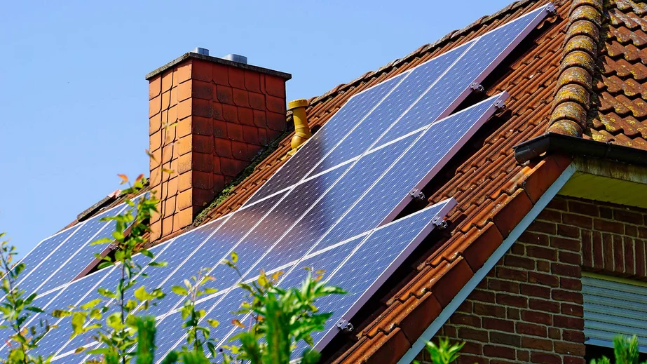 Hausdach mit schräger Dachneigung und Schornstein mit roten Dachziegeln in der Schrägansicht, das Dach ist zum größten Teil mit den Solarpanelen einer Photovoltaik-Anlage bedeckt.