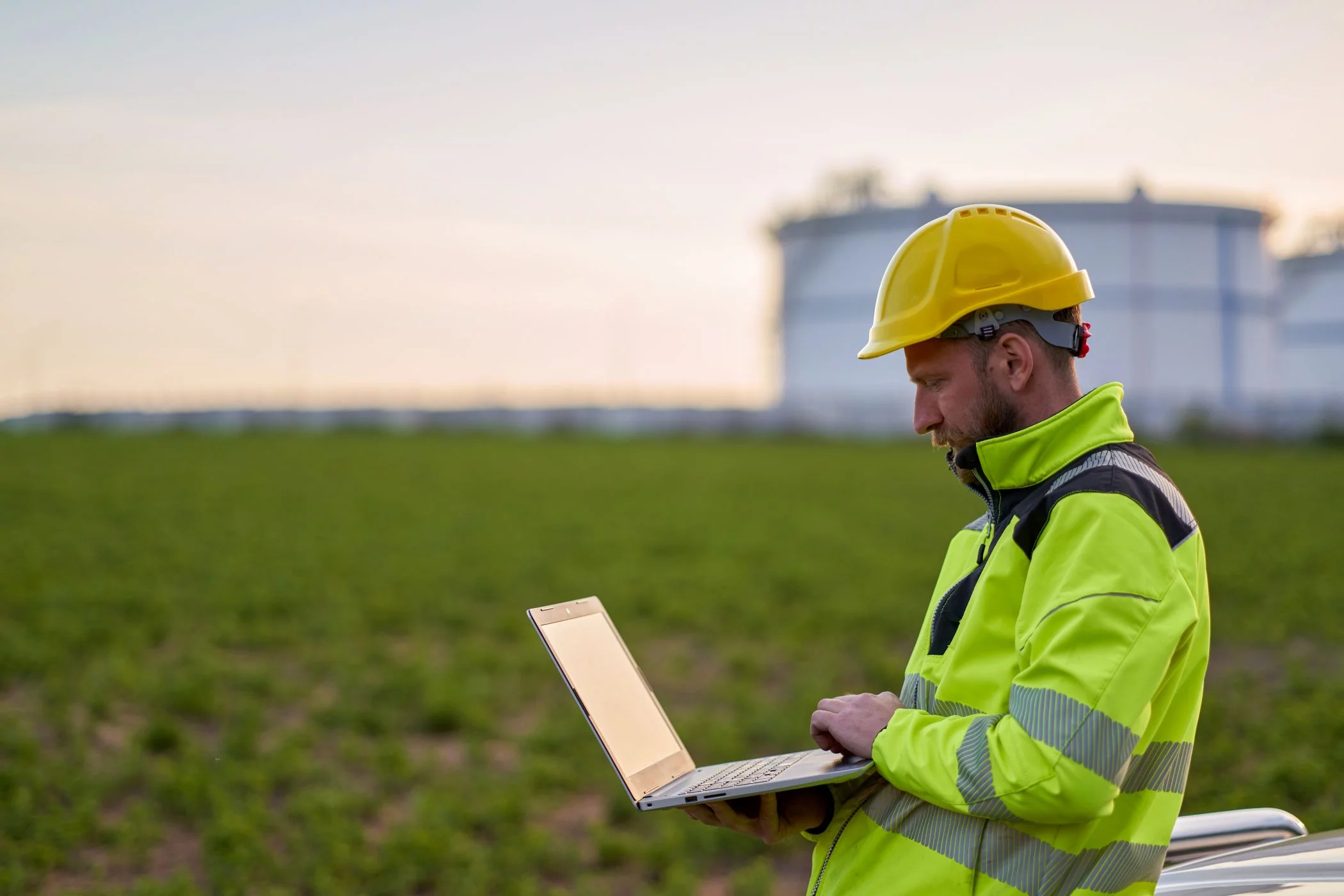 „Ein Mann in Sicherheitskleidung und gelbem Schutzhelm steht auf einem Feld und arbeitet mit einem Laptop