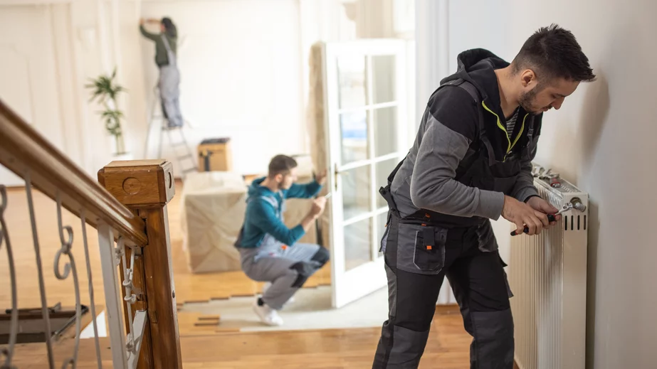 fg Handwerker führen Arbeiten in einem Altbau aus, im Vordergrund schraubt ein Handwerker an dem Ventil einer Heizung, als Symbolbild für das neue Heizungsgesetz.